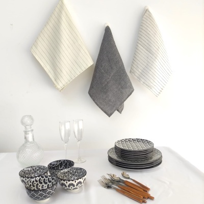 Panôs de cozinha às riscas e louça branca com padrões azuis e pretos numa mesa branca