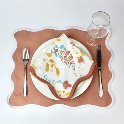 Conjunto de jantar com prato branco, guardanapo floral, base ondulada castanha e branca, talheres e taça