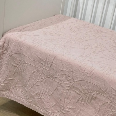 Colcha de cama rosa claro com padrão de folhas texturizadas sobre cama branca