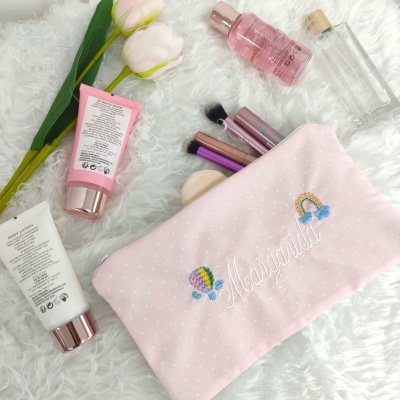Necessaire cor-de-rosa clara com bordados coloridos e acessórios de maquiagem e flores ao redor
