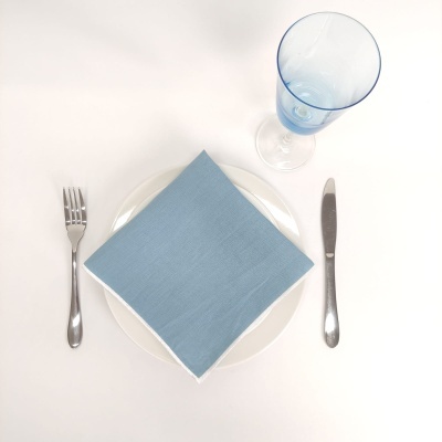 Mesa posta com prato branco, guardanapo azul, talheres metálicos e copo de vidro azul