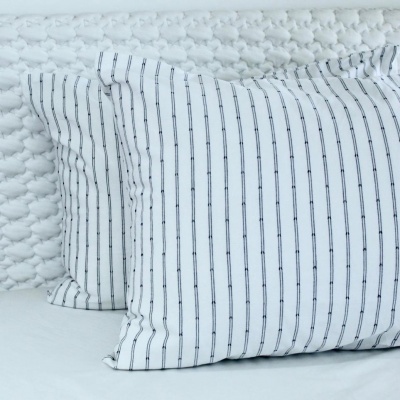 Duas almofadas com fronhas brancas e riscas pretas sobre superfície texturada branca