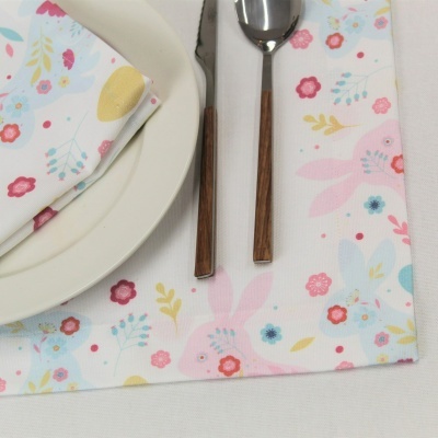 Guardanapos e toalha com padrão floral e coelhos, talheres com cabo de madeira e prato branco