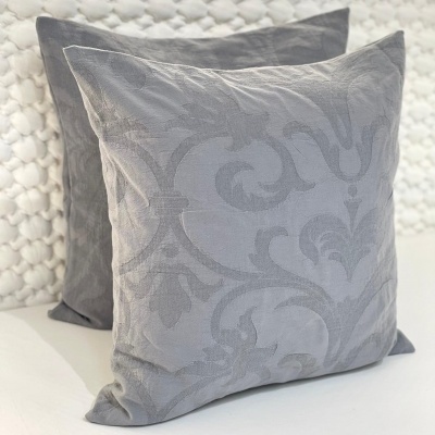 Duas almofadas cinzentas, uma com padrão floral em relevo e outra lisa, sobre superfície branca texturizada