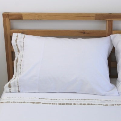 Almofada branca com bordado bege e castanho numa cama com cabeceira de madeira clara