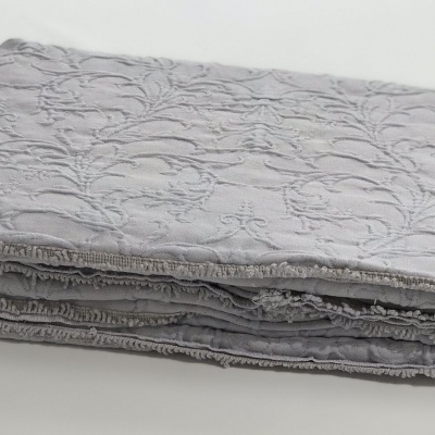 Colcha cinzenta clara com padrão floral texturizado dobrada