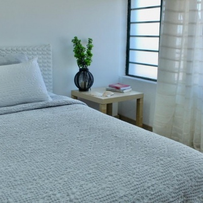 Cama de casal com roupa cinza texturizada numa decoração minimalista com mesa de cabeceira e planta