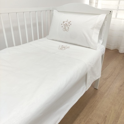 Cama de criança branca com lençóis brancos bordados com ursinho castanho
