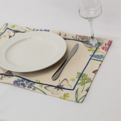 Individual de tecido com padrão floral, prato branco, faca metálica e copo de vidro