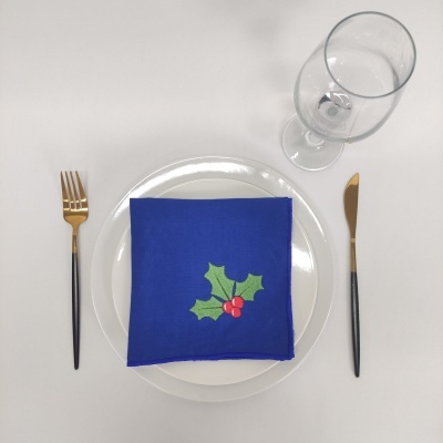 Conjunto de mesa com guardanapo azul bordado, prato branco, talheres dourados e copo transparente