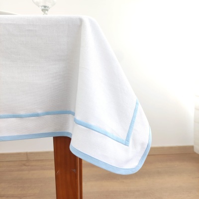 Toalha de mesa branca com borda azul pendurada numa mesa de madeira