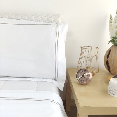 Cama com lençóis brancos e mesa de cabeceira com relógio de mesa e decoração