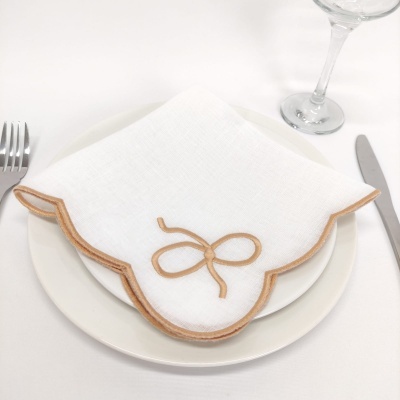 Guardanapo branco com borda castanho e bege e laço bordado sobre prato branco numa mesa com talheres e copo