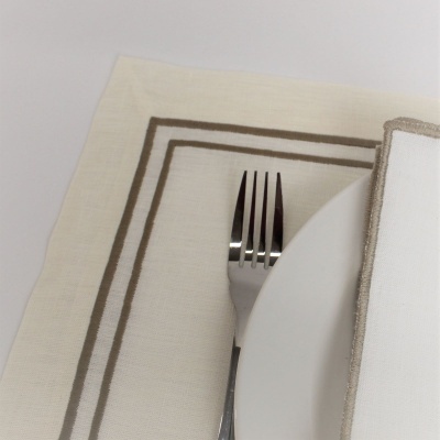 Guardanapo branco com bordas cinza sobre prato branco e garfo ao lado em toalha de mesa clara com linhas cinza