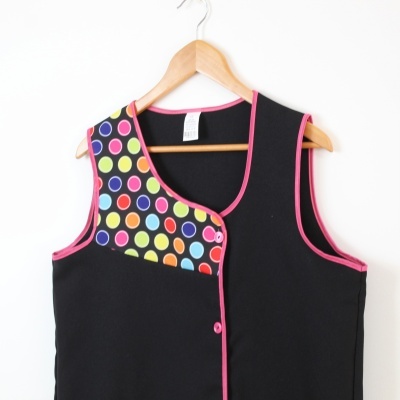 Colete preto com bolinhas coloridas no ombro esquerdo, detalhes rosa e botão rosa