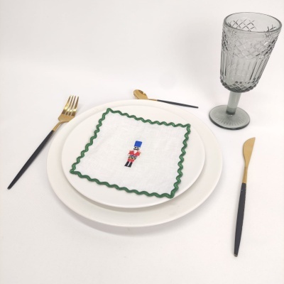 Mesa posta com guardanapo bordado de soldado de chumbo, prato branco, talheres dourados e pretos, e copo cinza