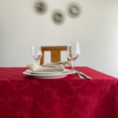 Mesa posta com toalha vermelha e pratos brancos, taças de vinho e talheres, cadeira de madeira e espelhos na parede
