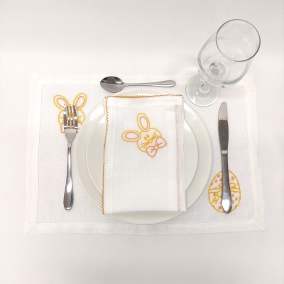 Jogo americano com desenhos de coelho e ovo, guardanapo com coelho, prato, talheres e copo em fundo branco