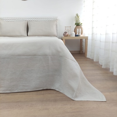 Cama com colcha e fronhas bege, mesa de cabeceira com decoração e cortinas brancas