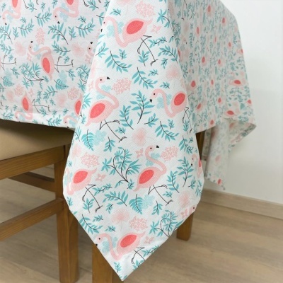 Toalha de mesa com padrão de flamingos e folhas pendurada numa mesa de madeira