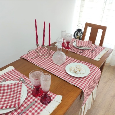Mesa posta com toalha e guardanapos xadrez vermelhos e brancos, copos rosa e castiçais com velas vermelhas