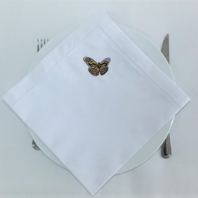 Guardanapo branco com bordado de borboleta sobre prato branco com talheres