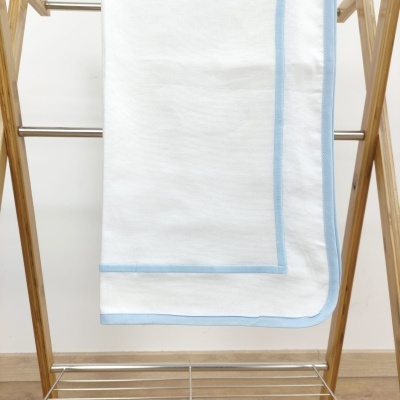 Manta branca com borda azul pendurada numa estrutura de madeira