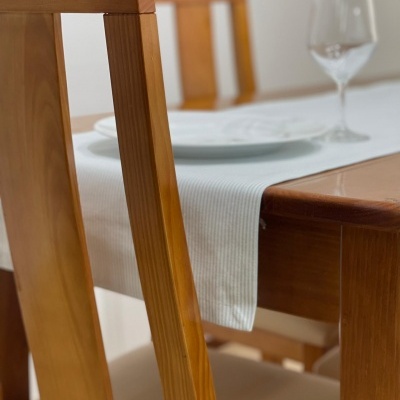 Mesa de madeira clara com cadeira, toalha branca, prato e copo de vidro