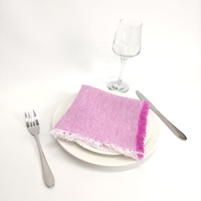 Mesa posta com prato branco, guardanapo rosa, garfo e faca metálicos e copo de vidro