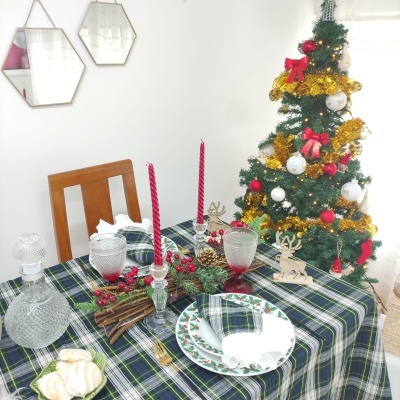 Mesa de jantar decorada com toalha xadrez e decoração de Natal, com árvore de Natal ao fundo