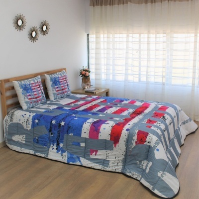 Colcha e fronhas coloridas com padrão geométrico em cama de madeira clara num quarto iluminado