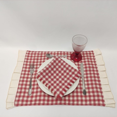 Conjunto de mesa com prato branco, talheres de aço, guardanapo e individual xadrez vermelho e branco, copo vermelho texturizado.