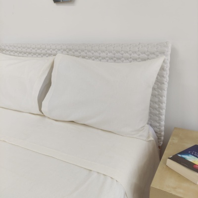 Conjunto de roupa de cama branco com cabeceira trançada e livros numa mesa de cabeceira