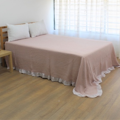 Colcha rosa com riscas brancas e barra ondulada branca sobre cama de madeira clara com almofadas brancas