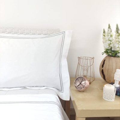 Jogo de cama branco com frisos cinza e mesa de cabeceira com flores e objetos decorativos