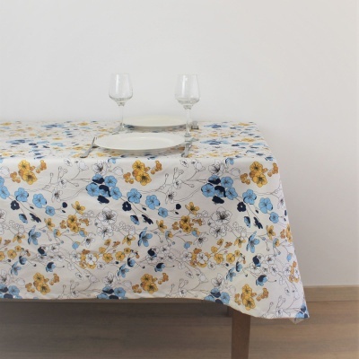 Toalha de mesa floral azul e amarelo sobre mesa de madeira com copos e prato
