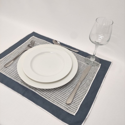 Lugar de mesa com pratos brancos, talheres de metal e uma taça sobre individual azul e cinza.