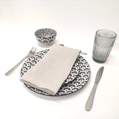 Conjunto de louça com padrão floral preto e branco, guardanapo bege, talheres prateados e copo de vidro texturizado