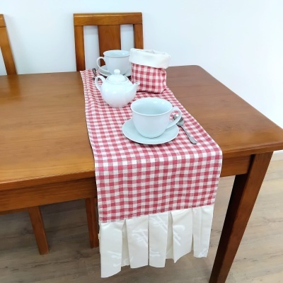 Toalha de mesa xadrez vermelho e branco com barra branca sobre mesa de madeira com jogo de chá branco