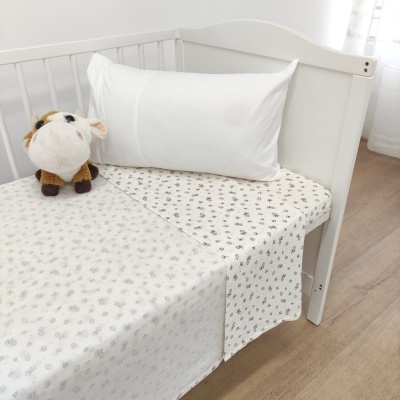 Berço branco com almofada branca, lençol estampado com flores castanhas e bege, peluche de vaca
