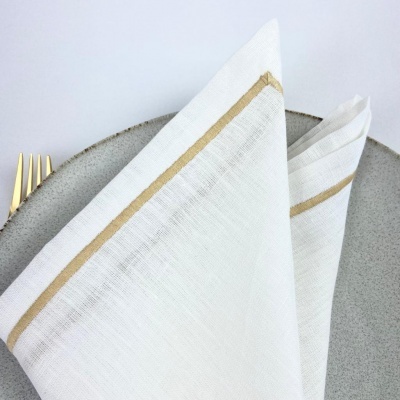 Guardanapo branco com riscas douradas sobre prato cinzento e garfos dourados