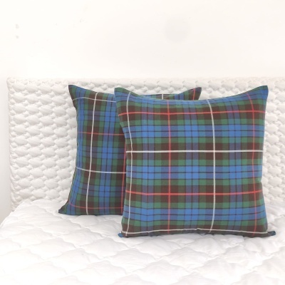 Duas almofadas com padrão xadrez azul e verde sobre manta branca acolchoada