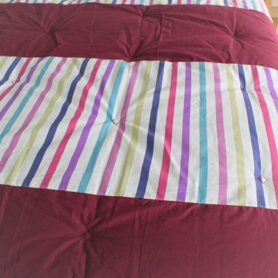 Edredão bordeaux com passadeira riscada colorida numa cama