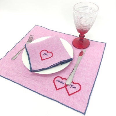 Jogo americano e guardanapo rosa com corações bordados, prato branco, talheres e copo rosa pontilhado