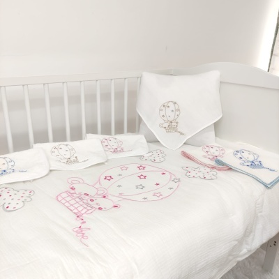 Fraldas e toalhas de bebé brancas bordadas com balões e estrelas num berço branco