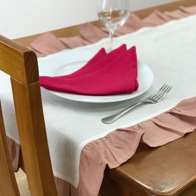 Toalha de mesa branca com borda rosa pregueada, mesa de madeira castanha clara, prato branco, guardanapo vermelho, copo vazio