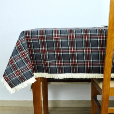 Toalha de mesa xadrez cinza, vermelho e branco com franjas brancas sobre mesa de madeira