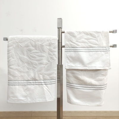 Toalhas brancas com padrão de folhas penduradas em suporte metálico prateado