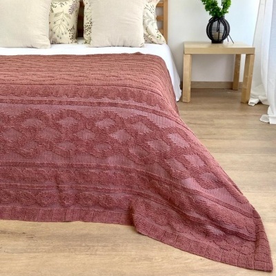 Colcha rosa texturizada sobre cama com almofadas e mesa com vaso