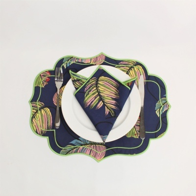 Jogo americano e guardanapo com padrão de folhas coloridas em tecido azul escuro com prato branco e talheres
